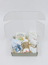 Curated Baby Git Box includes pair of shoes, socks, muslin wrap, book, beanie, onesie, teether, and stuffed animal blanket.