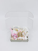 Curated Baby Git Box includes pair of shoes, socks, muslin wrap, book, beanie, onesie, teether, and stuffed animal blanket.