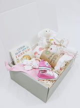 Curated Baby Git Box includes pair of shoes, socks, muslin wrap, book, beanie, onesie, teether, and stuffed animal blanket.