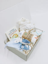 Curated Baby Git Box includes pair of shoes, socks, muslin wrap, book, beanie, onesie, teether, and stuffed animal blanket.