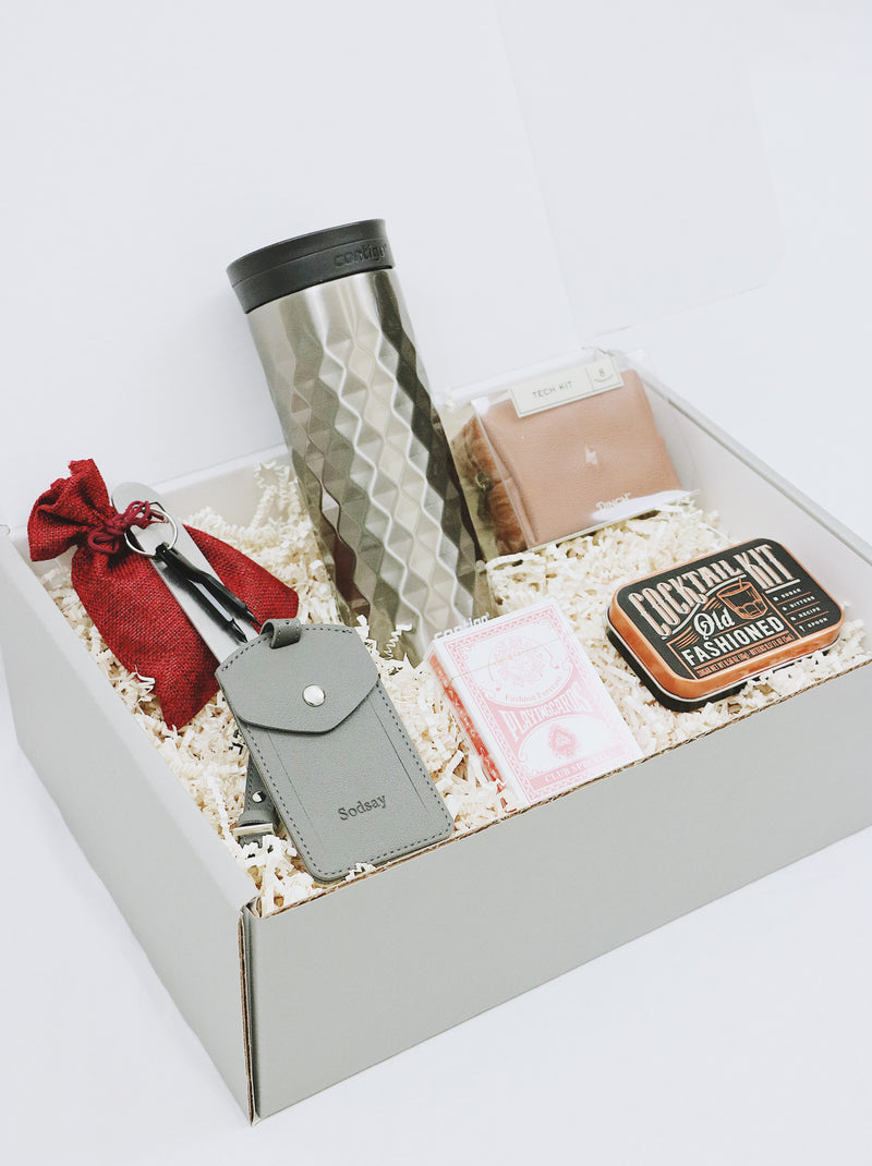 Personalized gift box for men with tech kit, old fashioned cocktail kit, playing cards, coffee tumbler, bottle opener, luggage tag, and unique keys as tools.
