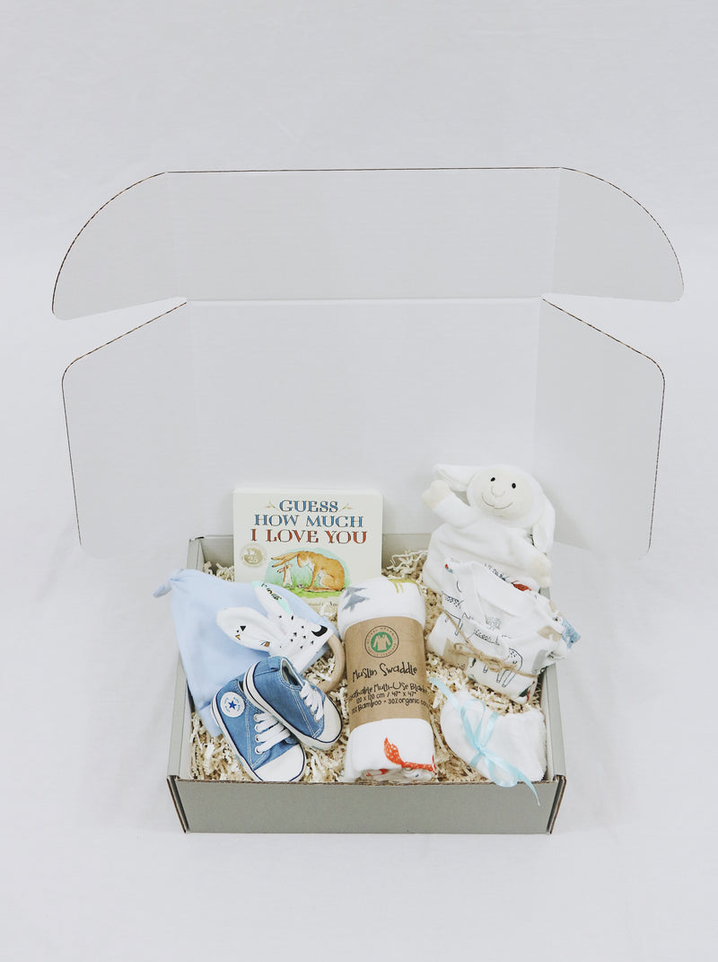 Curated Baby Git Box includes pair of shoes, socks, muslin wrap, book, beanie, onesie, teether, and stuffed animal blanket.
